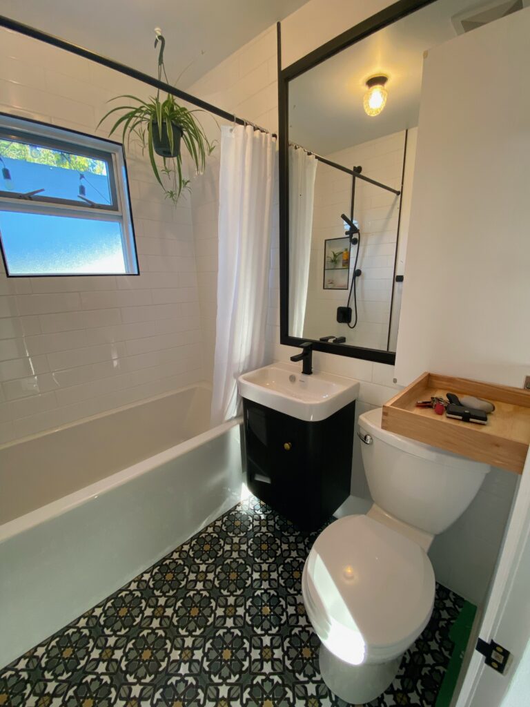 A bathroom space has green tiled floors and a small black cabinet under the sink.