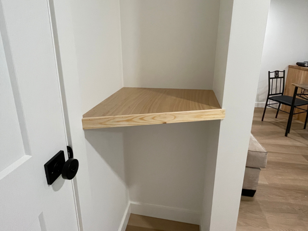 A small nook next to the front door of the studio apartment has a custom-built light wooden shelf.