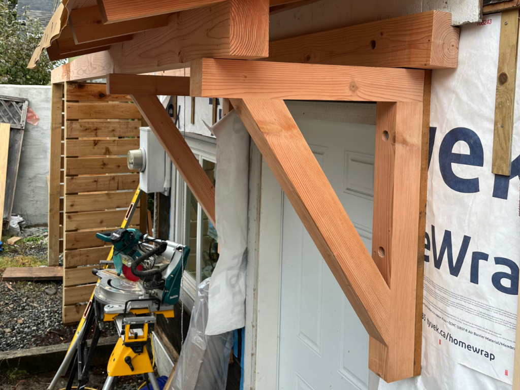 A knee brace structure is built out of warm coloured wood to support a front entry way addition.