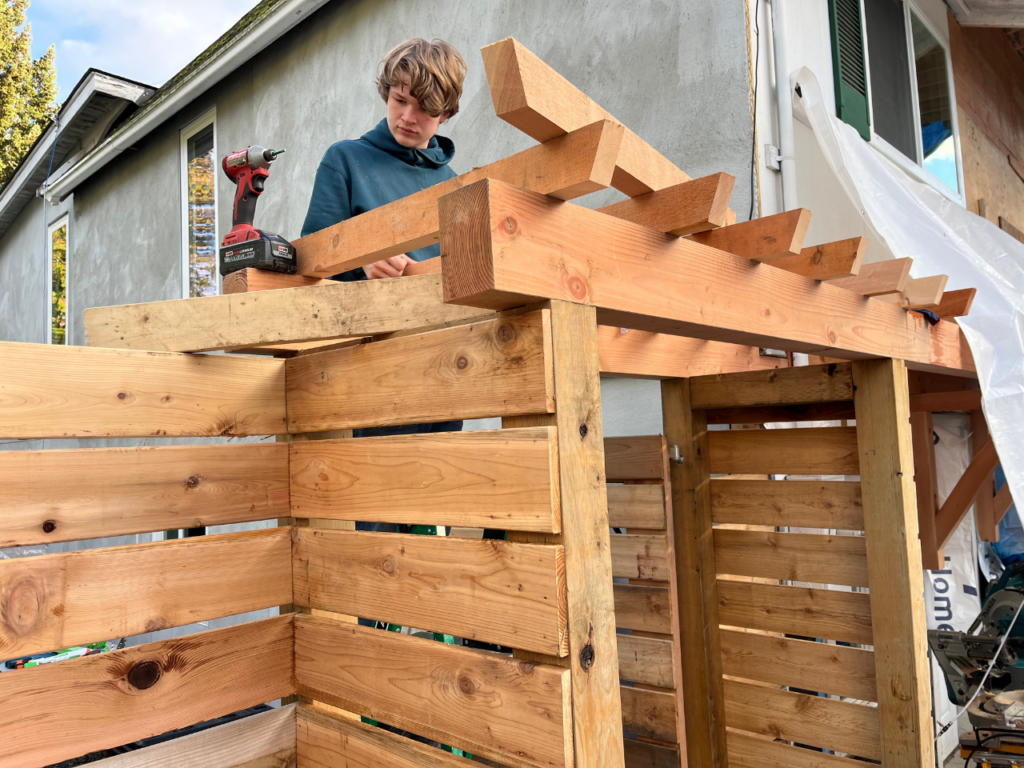 A young man is building a warm coloured wood gate entrance and fence.