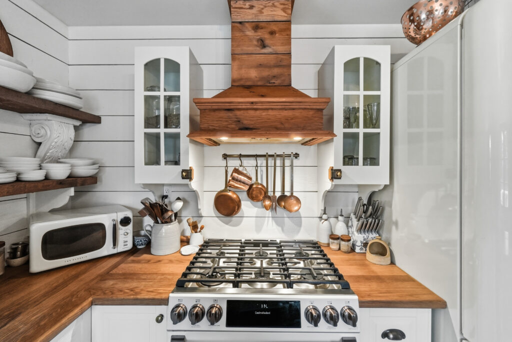 A wooden hood fan sits above the stove surrounded by wooden counters and white shiplap walls.