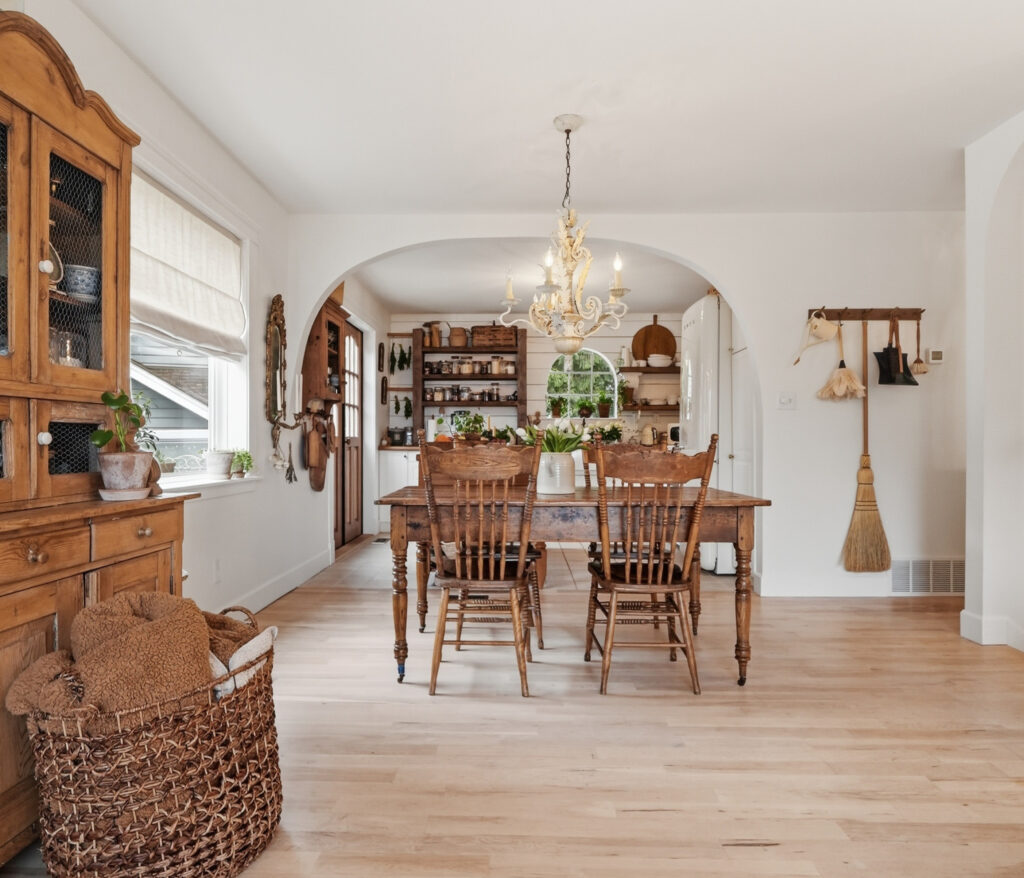 A dining room table and chairs are placed in front of an archway opening into the kitchen.
