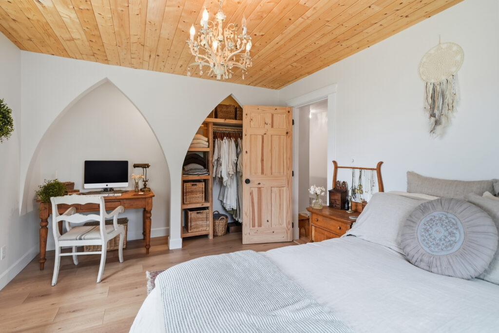 A bedroom has two carved arches in the wall. One opens to a desk and computer, the other to a closet and dresser.