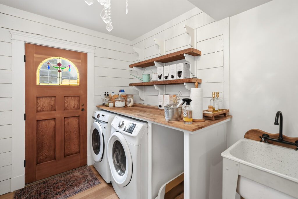 A laundry room with custom built counters, floating shelves, sink, and shiplap walls.